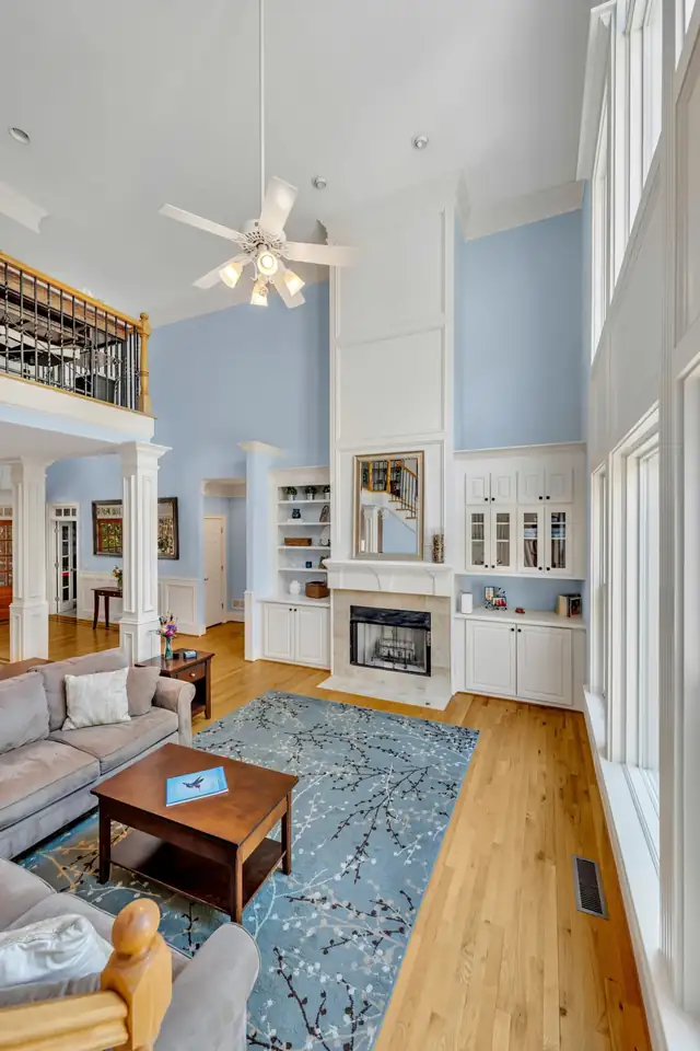 Two-story living room with built-in shelving, fireplace, ceiling fan and hardwood floors after a home remodel