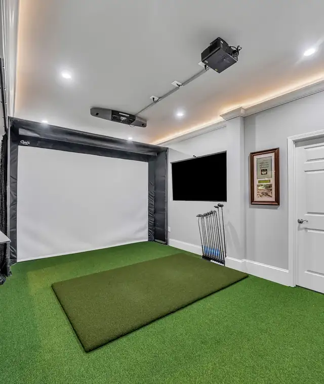Finished basement golf simulator room with green turf, impact screen and wall-mounted TV