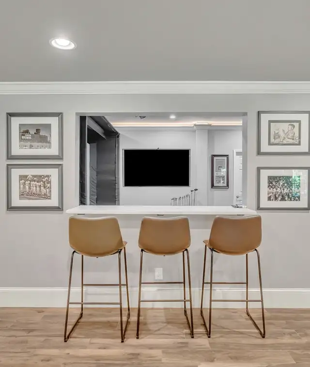 Finished basement bar counter with three leather stools, framed art and a pass-through to a TV room