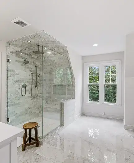 Walk-in shower with marble-look tile, frameless glass enclosure and rain showerhead beside a window