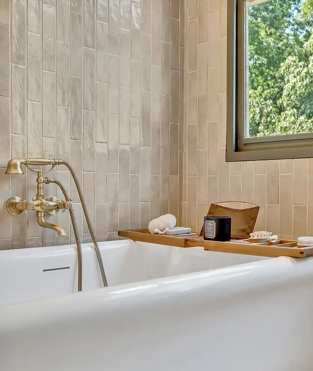 Freestanding tub with brass wall-mounted faucet, bath tray and handmade-look wall tile