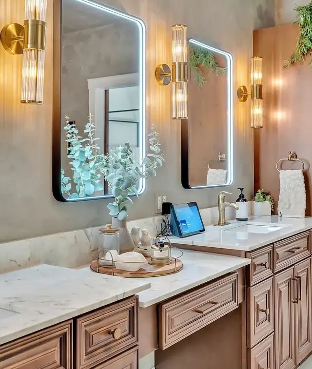 Bathroom vanity with stained wood cabinets, marble-look top, backlit mirror and brass wall sconces