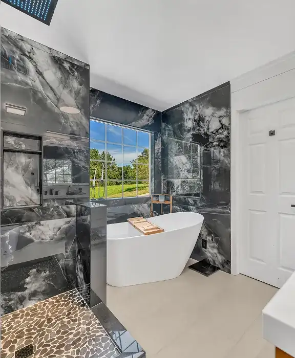 Shower with dark marble-look wall tile, pebble floor and a freestanding tub under a window