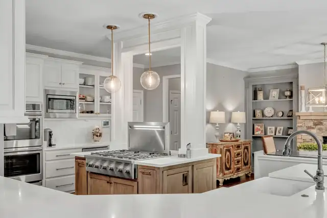 White kitchen with wood-stained island, stainless gas cooktop, glass pendant lights and built-in shelving