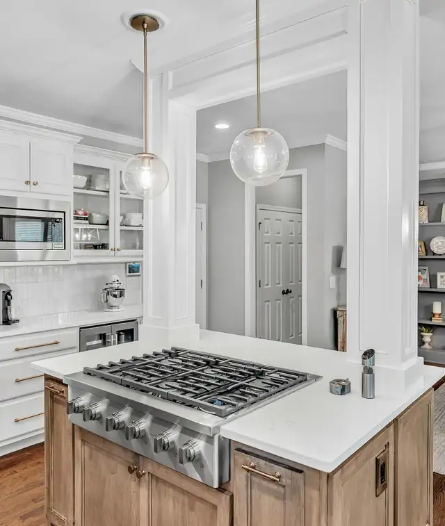 Kitchen by Integral Renovations with a stained wood island, a stainless gas cooktop, white quartz and glass globe pendants