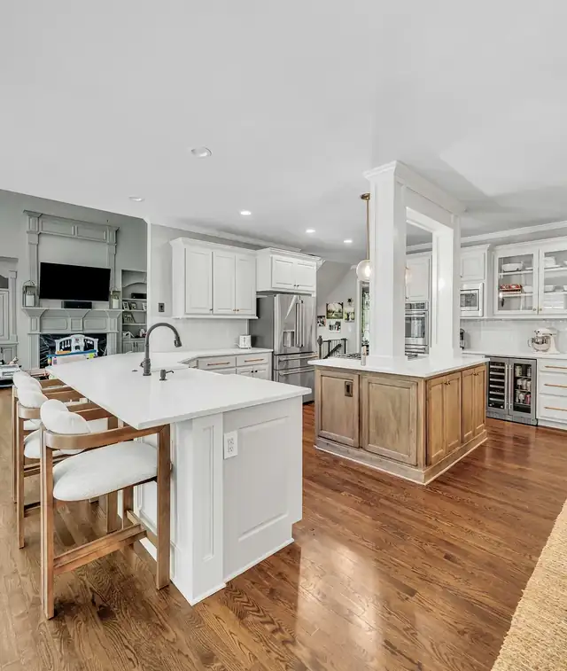 Open kitchen with white island seating, second wood-stained island, white cabinets and hardwood floors